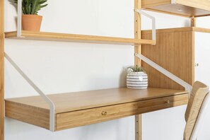 Uma escrivaninha de madeira com uma gaveta, um vaso de planta e um recipiente listrado.