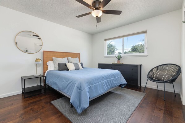 A bedroom with a bed, a nightstand, a dresser, a chair, a ceiling fan, a window, and a mirror.