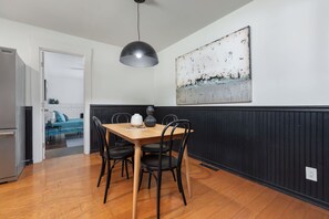 A dining area with a wooden table, black chairs, a pendant light, and a large abstract painting on the wall.