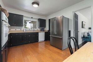 Une cuisine moderne avec des meubles de couleur sombre, un réfrigérateur en acier inoxydable et un plancher en bois.