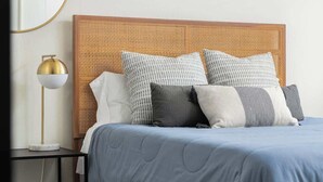 Ein ordentlich bezogenes Bett mit einer blauen Quilterdecke, einem Holz-Kopfteil und mehreren Kissen.