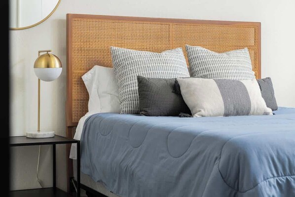 A neatly made bed with a blue quilt, a wooden headboard, and several pillows.