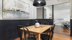 A dining area with a wooden table, black chairs, a black pendant light, and a large abstract painting on the wall.