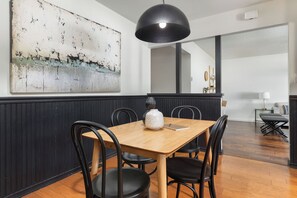 Uma área de refeições com mesa de madeira e cadeiras pretas, luminária pendente preta e uma grande pintura abstrata na parede.