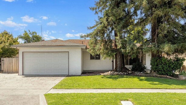 A single-story house with a garage, a well-maintained lawn, and a large tree in front.