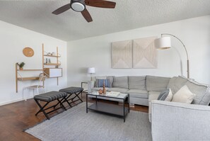Un salon moderne comprenant un canapé, une table basse, un pouf et un ventilateur de plafond.