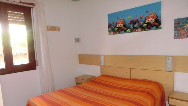 Quarto com cama, mesa de cabeceira, cabeceira de madeira e janela com cortinas.