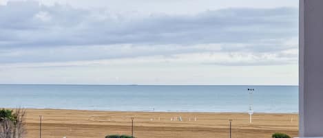 A beach view from a balcony with a clear sky, a sandy beach, and a lifeguard tower in the distance.