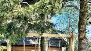 Um conjunto de baloiço de madeira numa área arborizada, com um edifício ao fundo.
