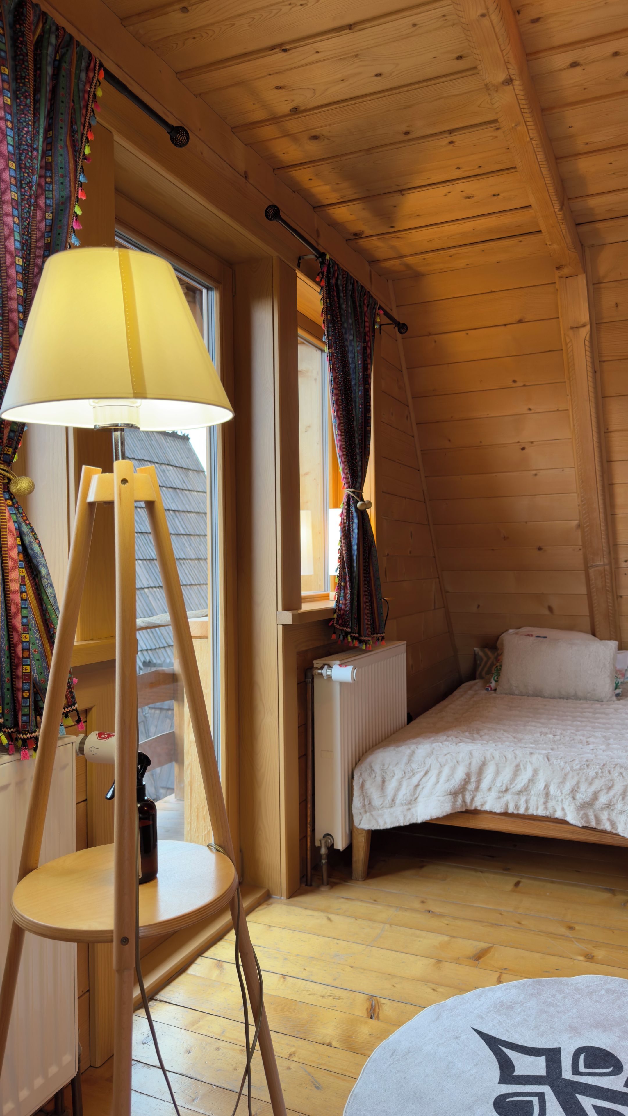 A cozy room with a bed, a lamp, a radiator, and a window with curtains.