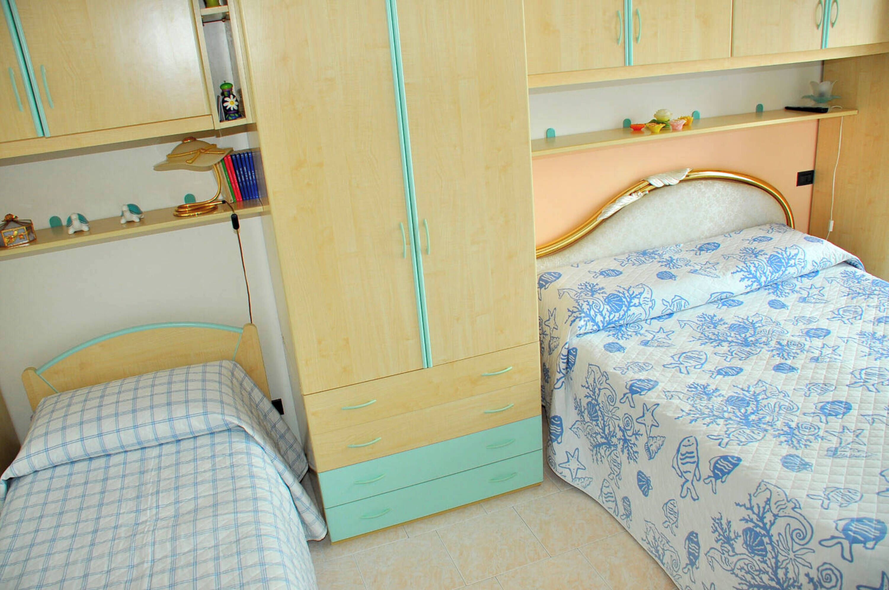 A bedroom with a bed, a wardrobe, and a shelf with books and decorative items.