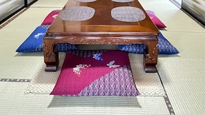 Une pièce avec un sol recouvert de tatamis, une table en bois, des coussins et une peinture japonaise traditionnelle.