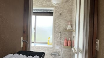 Une salle de bain avec une douche, un lavabo, un porte-serviettes et une fenêtre.