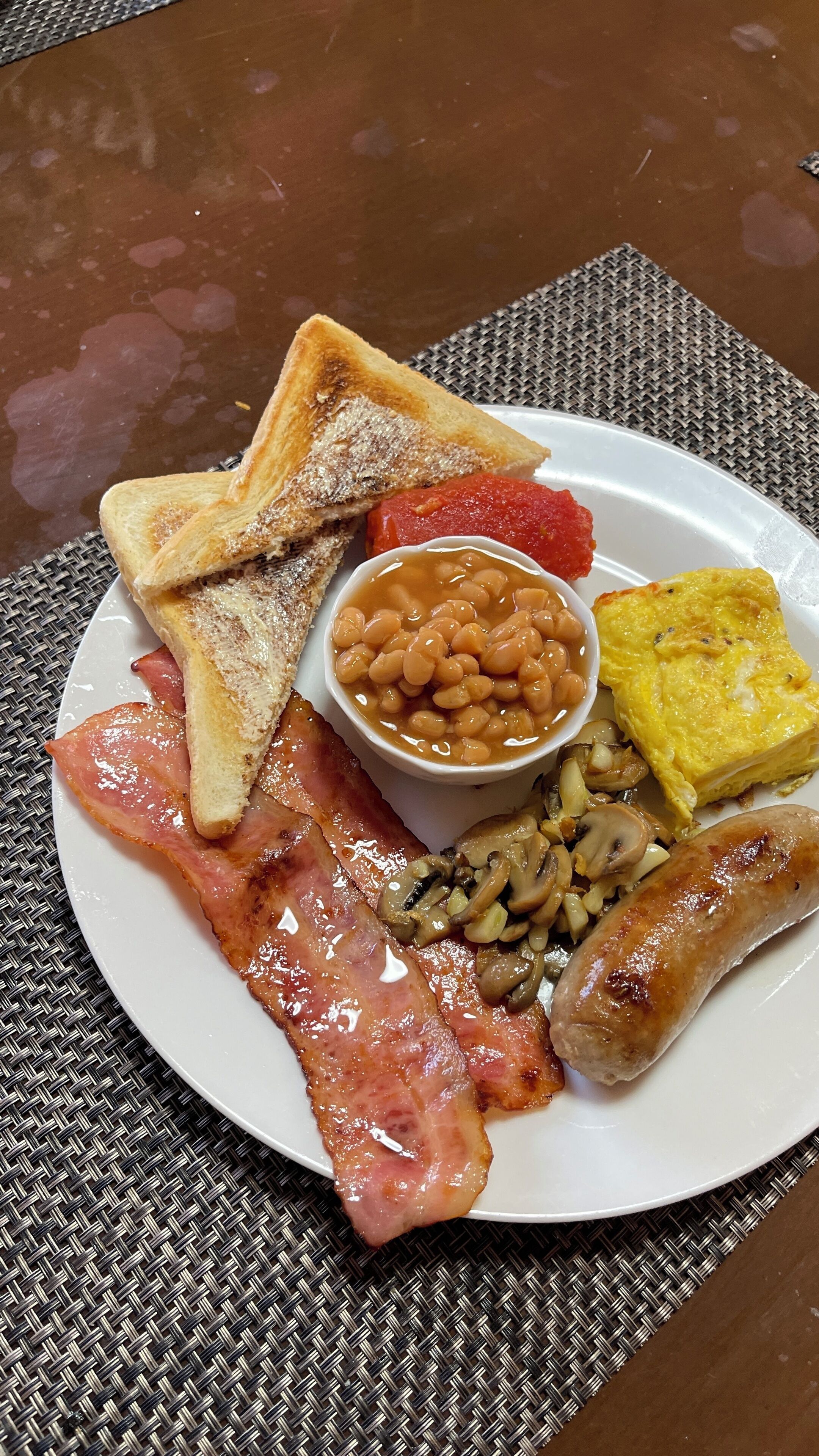 Um prato com torradas, feijão, bacon, cogumelos, salsichas e ovo frito.