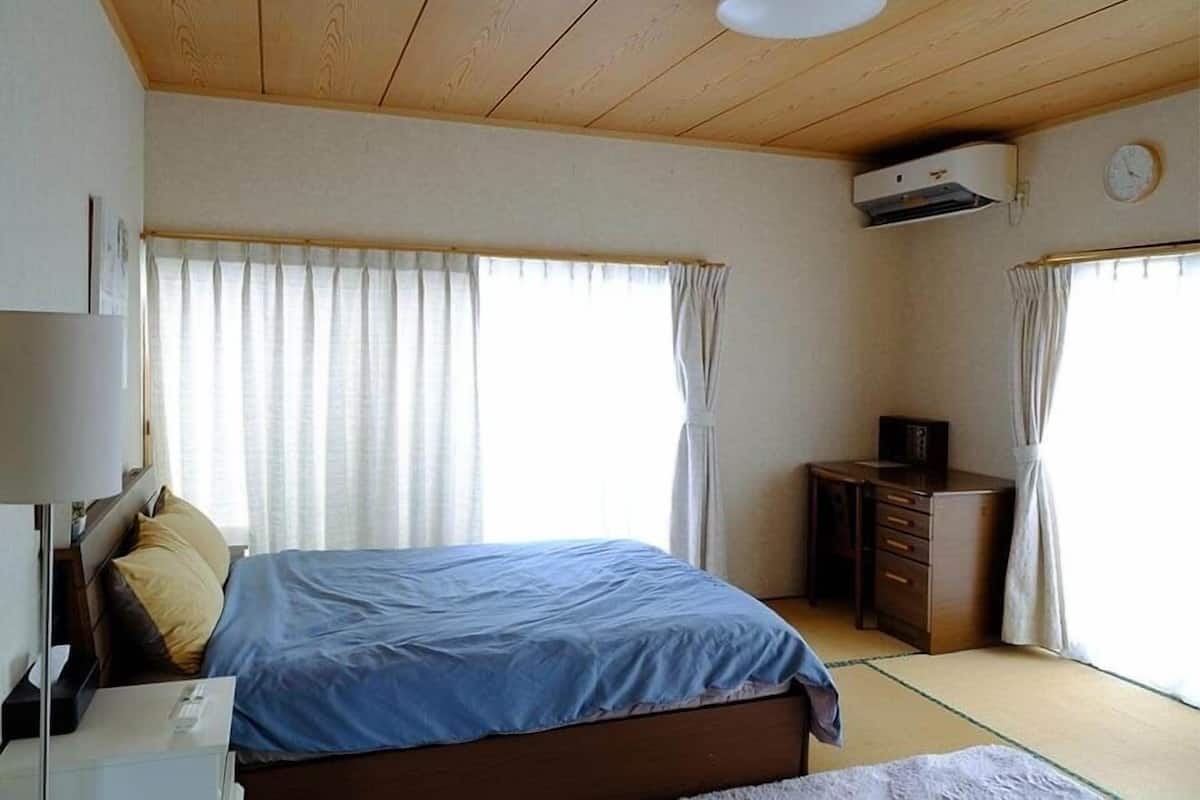 Une chambre avec un lit, un bureau et une armoire. Il y a une fenêtre avec des rideaux et un appareil de climatisation fixé au mur.