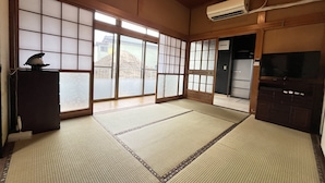 Une pièce de style japonais traditionnel, avec un sol recouvert de tatamis, des portes coulissantes, un téléviseur et un appareil de climatisation.