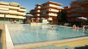 A swimming pool area with multiple levels of balconies, sun loungers, and umbrellas. - Nice Apartment in a Residence With Swimming Pool (San Michele al Tagliamento)
