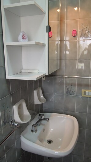 A bathroom with a white sink, a urinal, and a shelf with a soap dispenser. - Nice Apartment in a Residence With Swimming Pool (San Michele al Tagliamento)