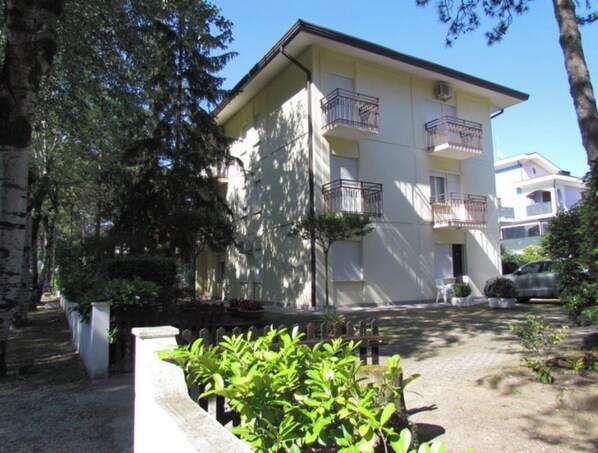 Un edificio de varios pisos con balcones, rodeado de árboles y un pequeño jardín.