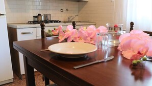 Una cocina con azulejos blancos, una estufa y un lavabo. Hay una mesa de comedor con un plato, un cuchillo y flores rosas.