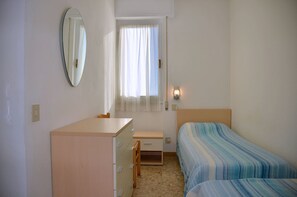 A small, clean room with a bed, a desk, a chair, a dresser, a mirror, and a window with curtains.
