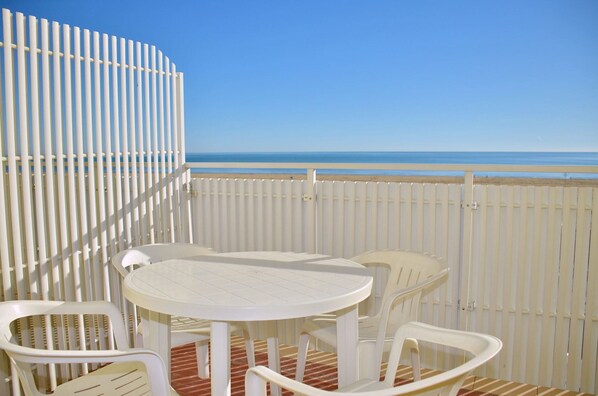 A balcony with a white table and chairs, overlooking a beach.