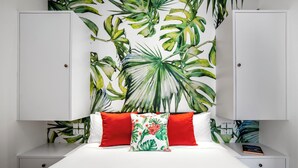 A bedroom with a white bed, red and white pillows, and a tropical leaf wallpaper. - Villa Balik II Seminyak (Seminyak)
