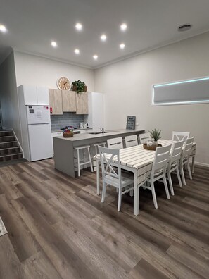 A modern kitchen with white cabinetry, a central island with seating, and a built-in oven. - Lakeside Coongulla - Waterfront Holiday Home - Sleeps 10 + (Coongulla)