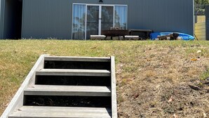 Ein zweistöckiges Gebäude mit einem großen Balkon, einer Schiebetür aus Glas und einer Holztreppe, die zum Eingang führt.
