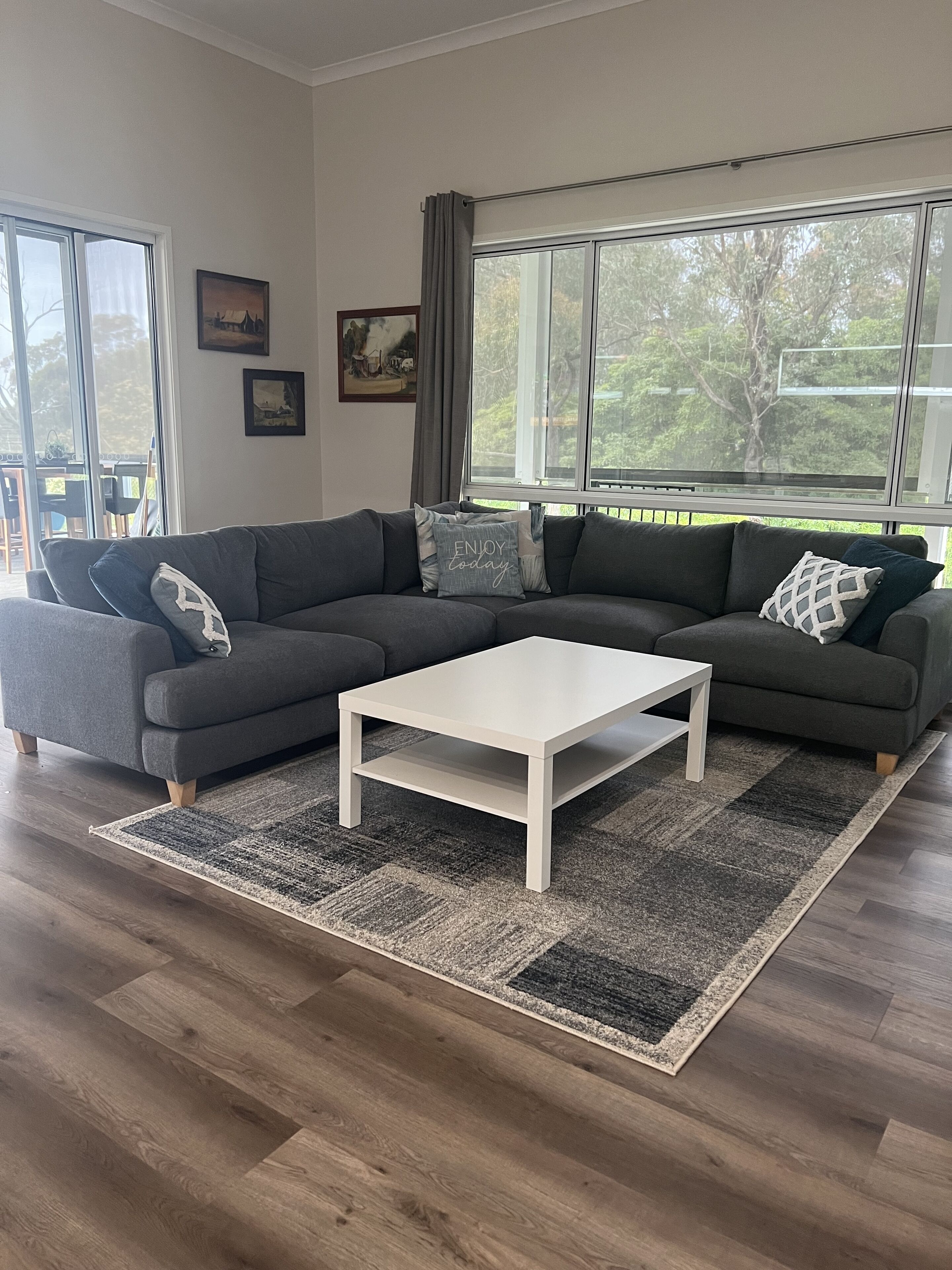 A modern living room with a sectional sofa, a white coffee table, and a large window with a view of trees.