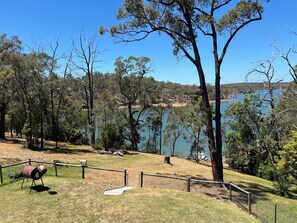 A fenced park area with a barbecue grill, a wooden bench, and a view of a lake surrounded by trees.