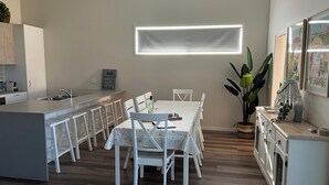 Eine moderne Küche mit einer zentralen Kochinsel, weißen Barhocker und einem Esstisch für sechs Personen.