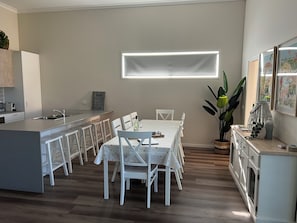 A modern kitchen with a central island, white bar stools, and a dining table set for six.