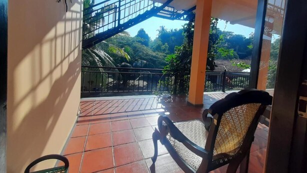Varanda coberta com cadeira, guarda-corrimão de metal e vista para uma escadaria que dá para um jardim.