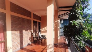Varanda coberta com piso de azulejos, parede de tijolos e guarda-corpo de metal.