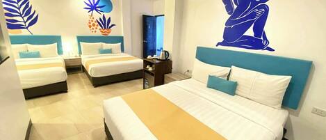 A hotel room with three beds, a large wall mural, and a desk with a chair.