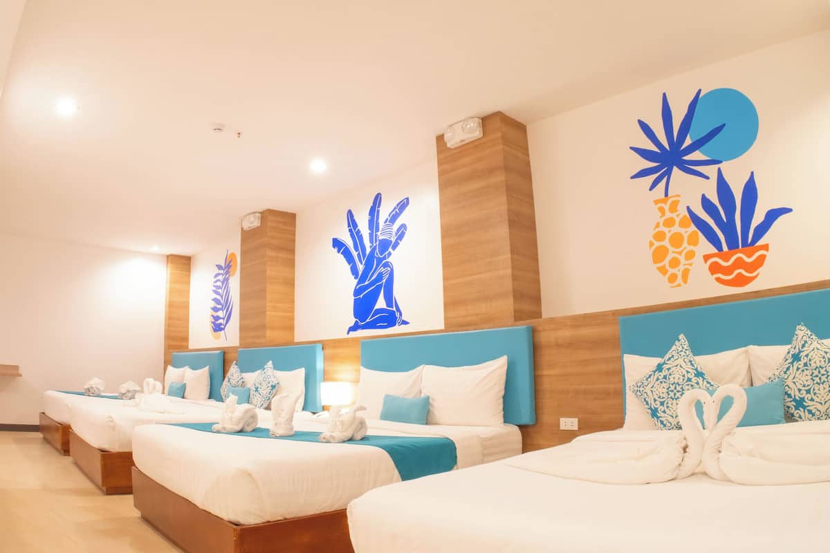 A hotel room with three beds, each with white linens and blue headboards. The room has wooden paneling on the walls and a large wall art piece above the beds.