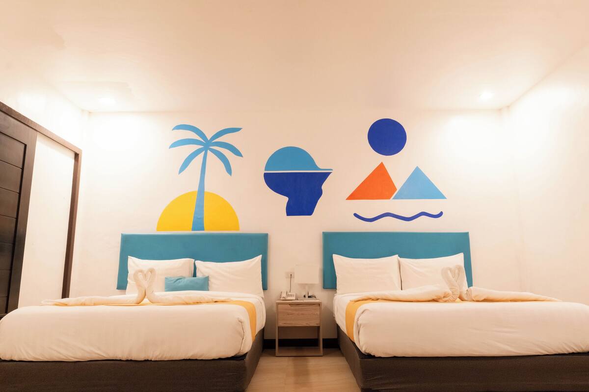 A hotel room with two beds, a nightstand, and a wall with a beach-themed mural.