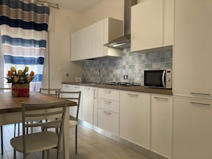 A modern kitchen with white cabinets, a tiled backsplash, a microwave, and a dining area with chairs and a table.