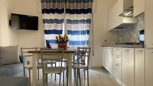 A modern kitchen with white cabinets, a flat-screen TV, and a dining area with a table and chairs. - Bright Apartment Close to the Beach (Rosolina)