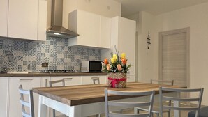 A modern kitchen with white cabinets, a patterned backsplash, and a wooden dining table with chairs. - Bright Apartment Close to the Beach (Rosolina)