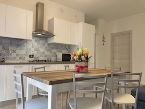 Une cuisine moderne avec des armoires blanches, un pare-feu décoratif, une hotte de cuisinière en acier inoxydable, un four à micro-ondes et une table à manger avec des chaises.