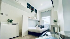 Een kleine hotelkamer met een bed, een bureau, een stoel, een raam en een bloempot.