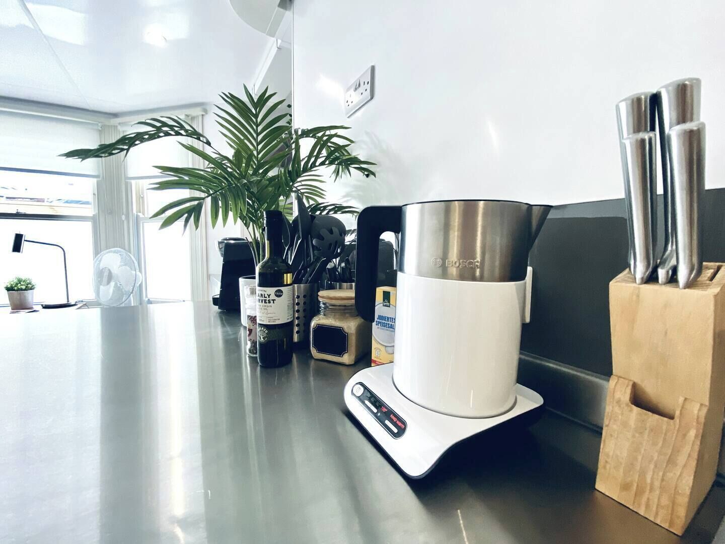 Eine Küchenarbeitsplatte mit einer Bosch-Kaffeemaschine, einer Pflanze, einer Waage und einem Messerblock.