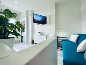 Ein modernes Wohnzimmer mit einem blauen Sofa, einem flachbildfernseher an der Wand und einer Zimmerpflanze.
