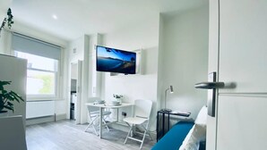 Een moderne, compacte woonruimte met kitchenette, eethoek, televisie aan de muur en een bank.