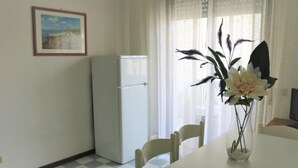 A dining area with a table, chairs, a refrigerator, and a vase with flowers. - Minimalist Apartment in a Quiet Area - Beahost (San Michele al Tagliamento)