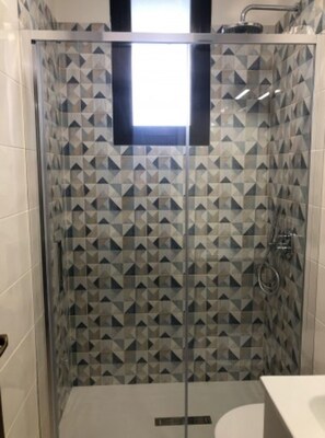 Eine Dusche mit geometrisch gemusterten Fliesen, einer Glastür und einem sichtbaren Duschkopf.