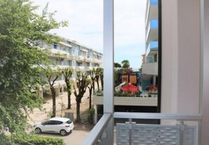 En bostadsbyggnad med balkonger, en parkerad bil framför och en lekplats med ett rött tak.