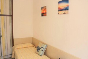 Una piccola camera con un letto singolo, una porta a righe, due quadri appesi alle pareti e un solo cuscino sul letto.